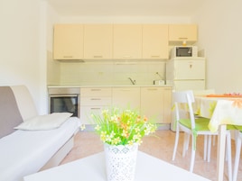 Cocina compacta con microondas, horno y refrigerador. Hay un comedor con mesa y sillas, y un sofá en la sala.