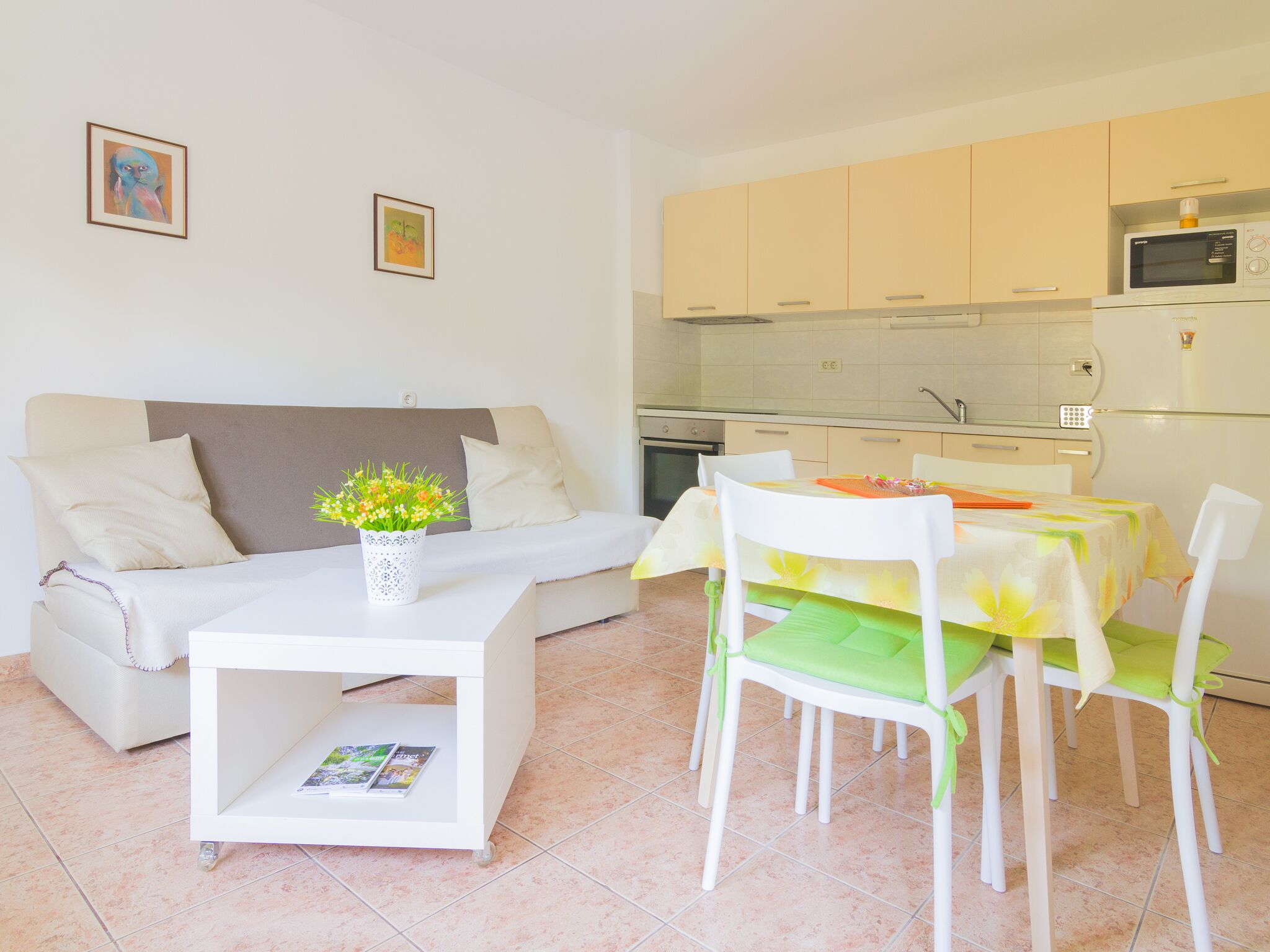 A modern living room with a sofa, a small table with a vase of flowers, and a dining area with a table and chairs.