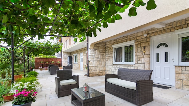 Un espace extérieur aménagé en terrasse, avec des meubles en osier, des plantes en pot et un bâtiment en pierre en arrière-plan.