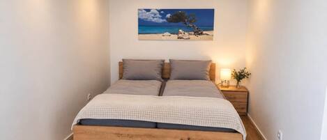 A bedroom with a bed, a nightstand, a lamp, and a painting of a beach scene.