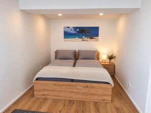 A bedroom with a bed, a nightstand, a lamp, and a painting of a beach scene.
