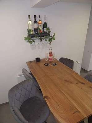 Een eetgedeelte met een houten tafel, vier stoelen en een wijnrek met flessen en glazen.