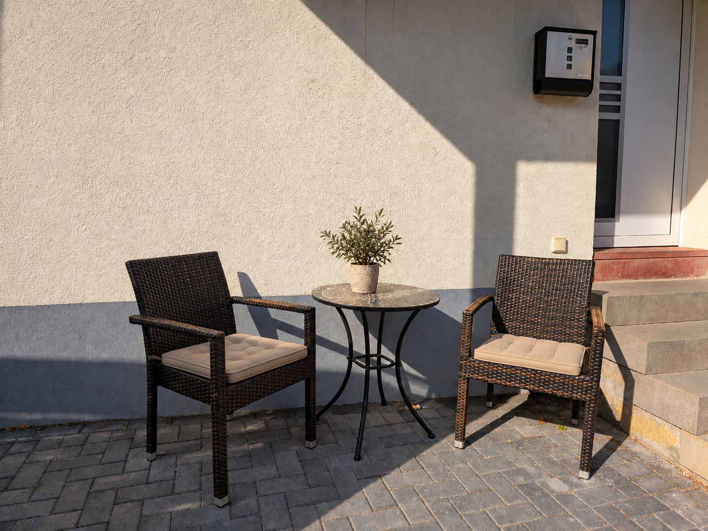 Deux fauteuils en osier avec des coussins, une petite table ronde et une plante en pot.