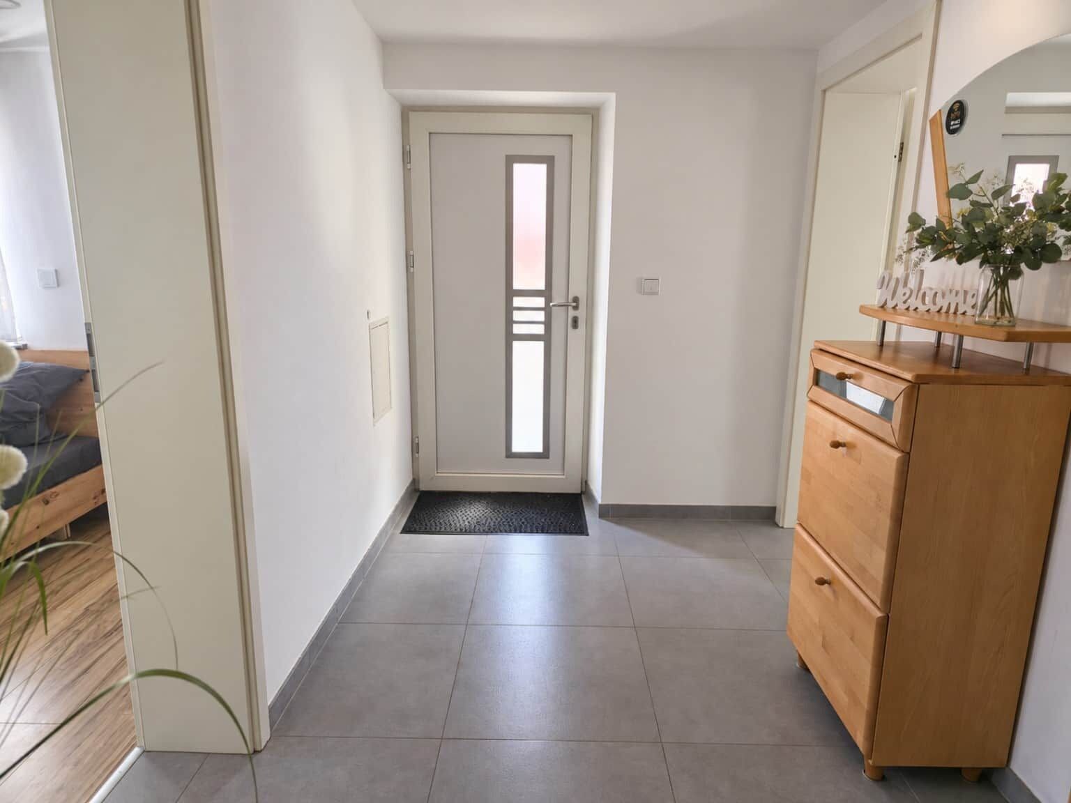A hallway with a wooden dresser, a door with a frosted glass panel, and a doormat.