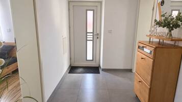 A hallway with a wooden dresser, a door with a frosted glass panel, and a doormat.
