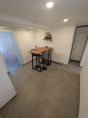 Een gezellig eetgedeelte met een houten tafel en vier stoelen, een fles rode wijn en een wijnglas op tafel.