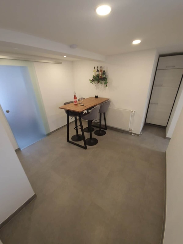 Un petit coin repas avec une table en bois et quatre chaises, une bouteille de vin rouge et un verre à vin posés sur la table.