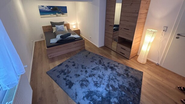 A bedroom with a bed, a wardrobe, a bedside table, a lamp, and a painting on the wall. - Modern vacation apartment in Altertheim near kist Würzburg highway A3 A81 (Altertheim)
