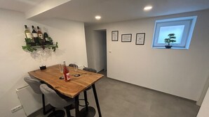 A dining area with a wooden table, chairs, and a wine bottle. There are wine bottles on a shelf above the table. - Modern vacation apartment in Altertheim near kist Würzburg highway A3 A81 (Altertheim)