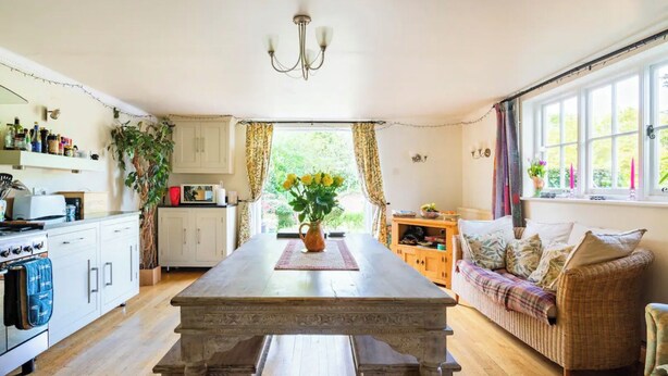A kitchen with a dining table, a sofa, and a window with curtains. - The Tallow Factory - Historic Tudor Home in Dedham (Dedham)