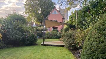 A garden with a wooden deck, a red building with a tower, and a large tree.
