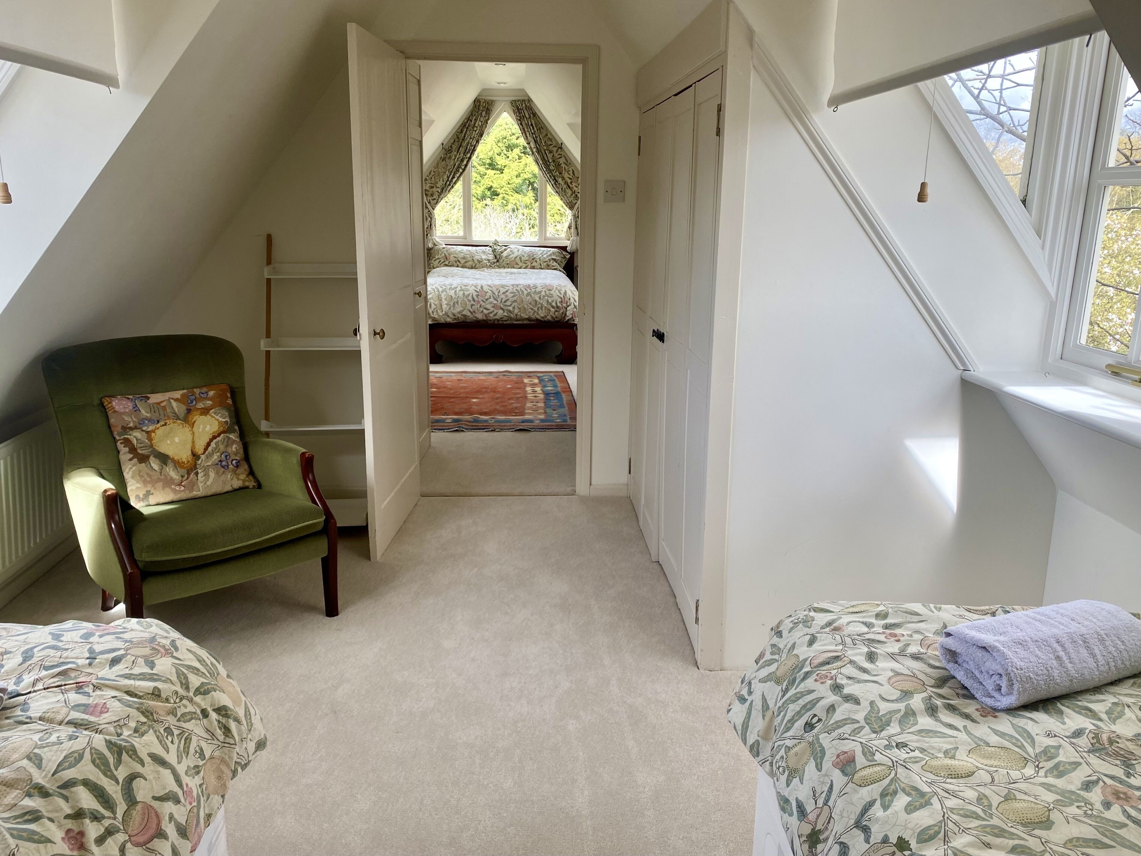 A bedroom with a loft bed, a green armchair, and a view through a window.