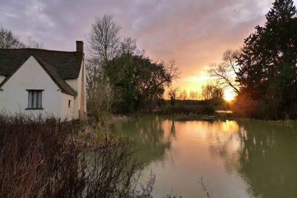 A white house with a gabled roof near a calm body of water reflecting the sunset.