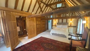 A bedroom with a large bed, a wooden wardrobe, a red patterned rug, and a wooden chair. - The Tallow Factory - Historic Tudor Home in Dedham (Dedham)