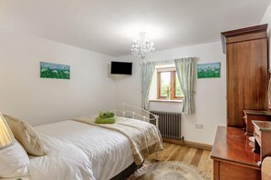 A bedroom with a bed, a radiator, a TV, a wooden wardrobe, and a window with curtains. - 2 Bed in Torrington (oc-p27344) (Langtree)
