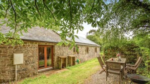 A stone house with a patio, a table with chairs, and a grill.