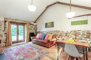 A cozy living room with a stone wall, a leather sofa, a dining table with chairs, and a large rug. - 2 Bed in Torrington (oc-p27344) (Langtree)