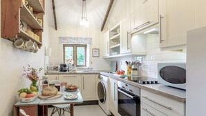 A kitchen with white cabinets, a microwave, a sink, and a window with a view of greenery.