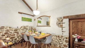 A dining area with a stone wall, wooden ceiling beams, a hanging light fixture, and a wooden door.