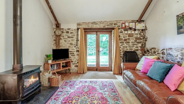 A cozy living room with a stone wall, a fireplace, a sofa with colorful cushions, and a television.