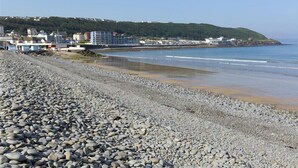 A pebbled beach with buildings in the background.