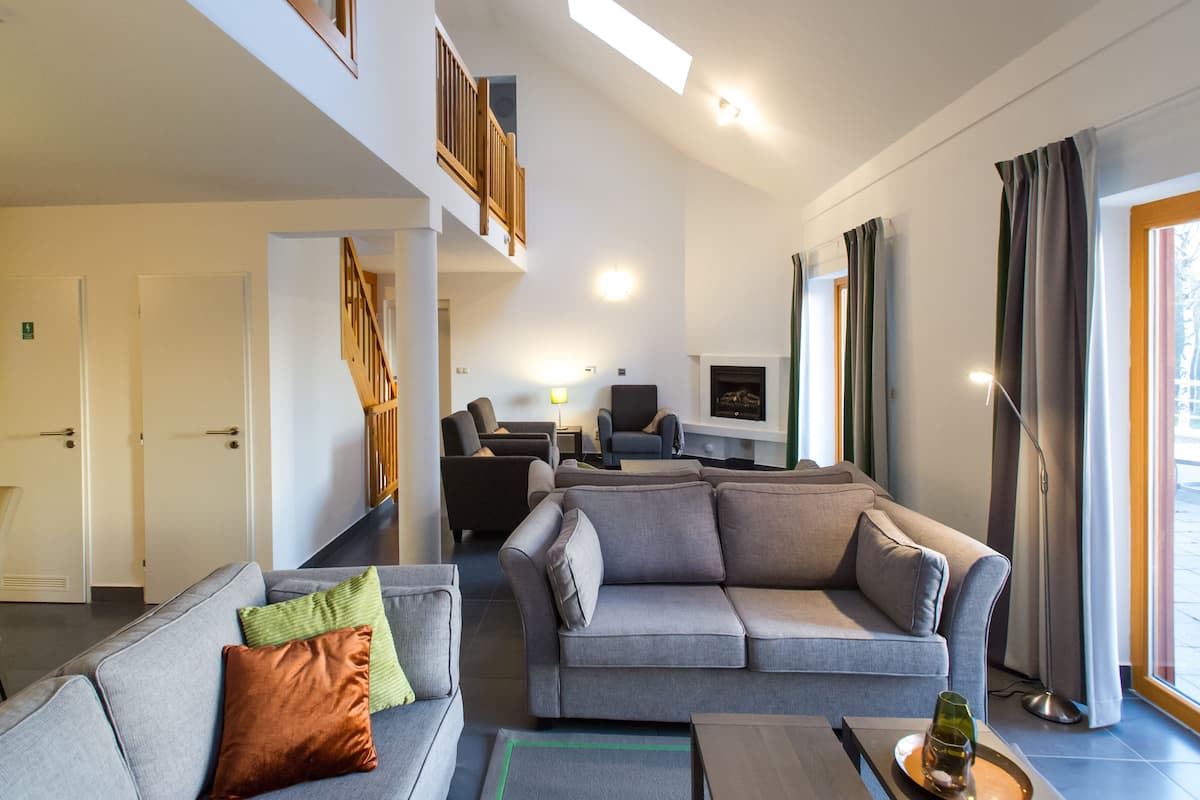 Amplia sala de estar con un sofá gris, una mesa de centro y una chimenea. Una escalera conduce a un nivel superior.