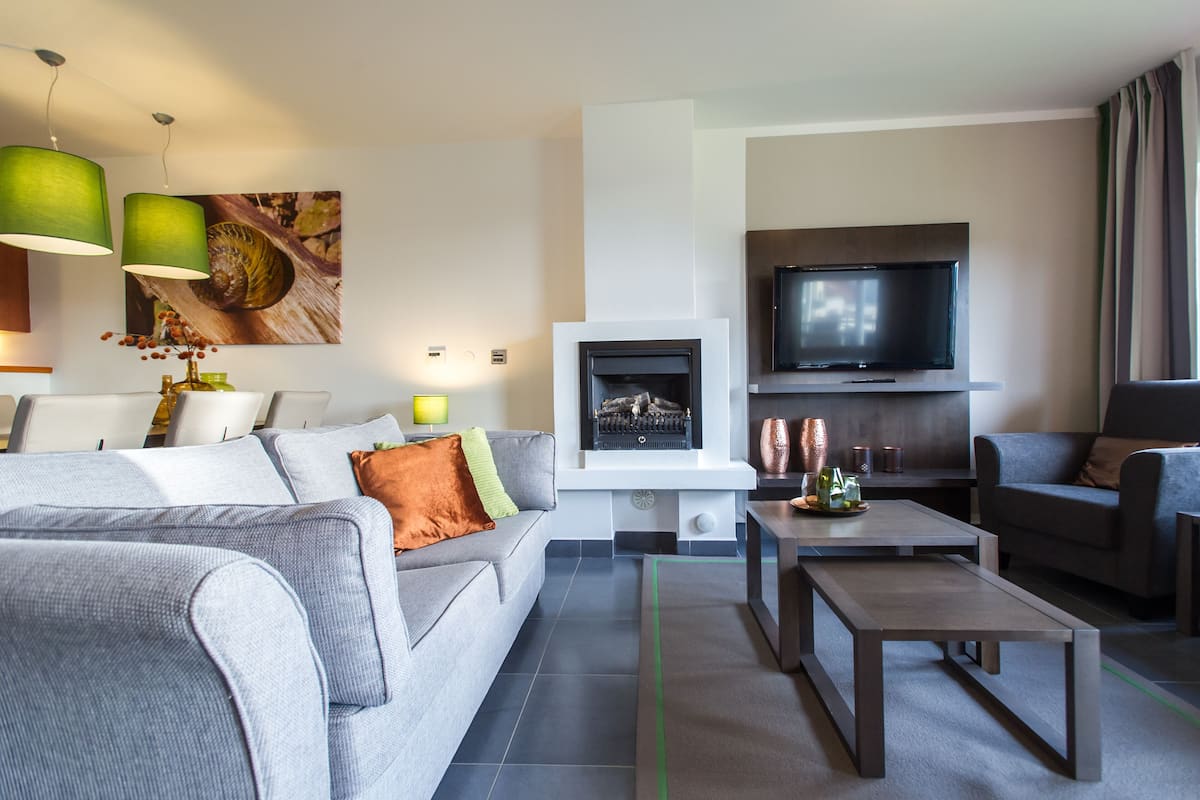 Una sala de estar moderna con chimenea, un televisor de pantalla plana, sofás grises y una mesa de centro.