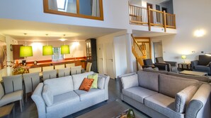 Un vaste espace de vie doté d’un haut plafond, un coin repas avec des chaises modernes et un escalier menant à un niveau supérieur.