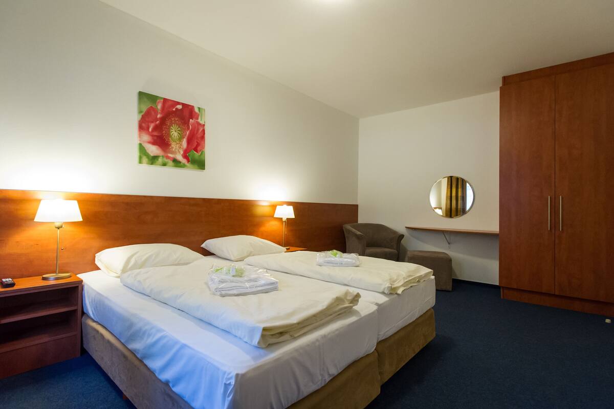 Habitación de hotel con dos camas, cabecero de madera, espejo redondo, escritorio con lámpara y un amplio armario.