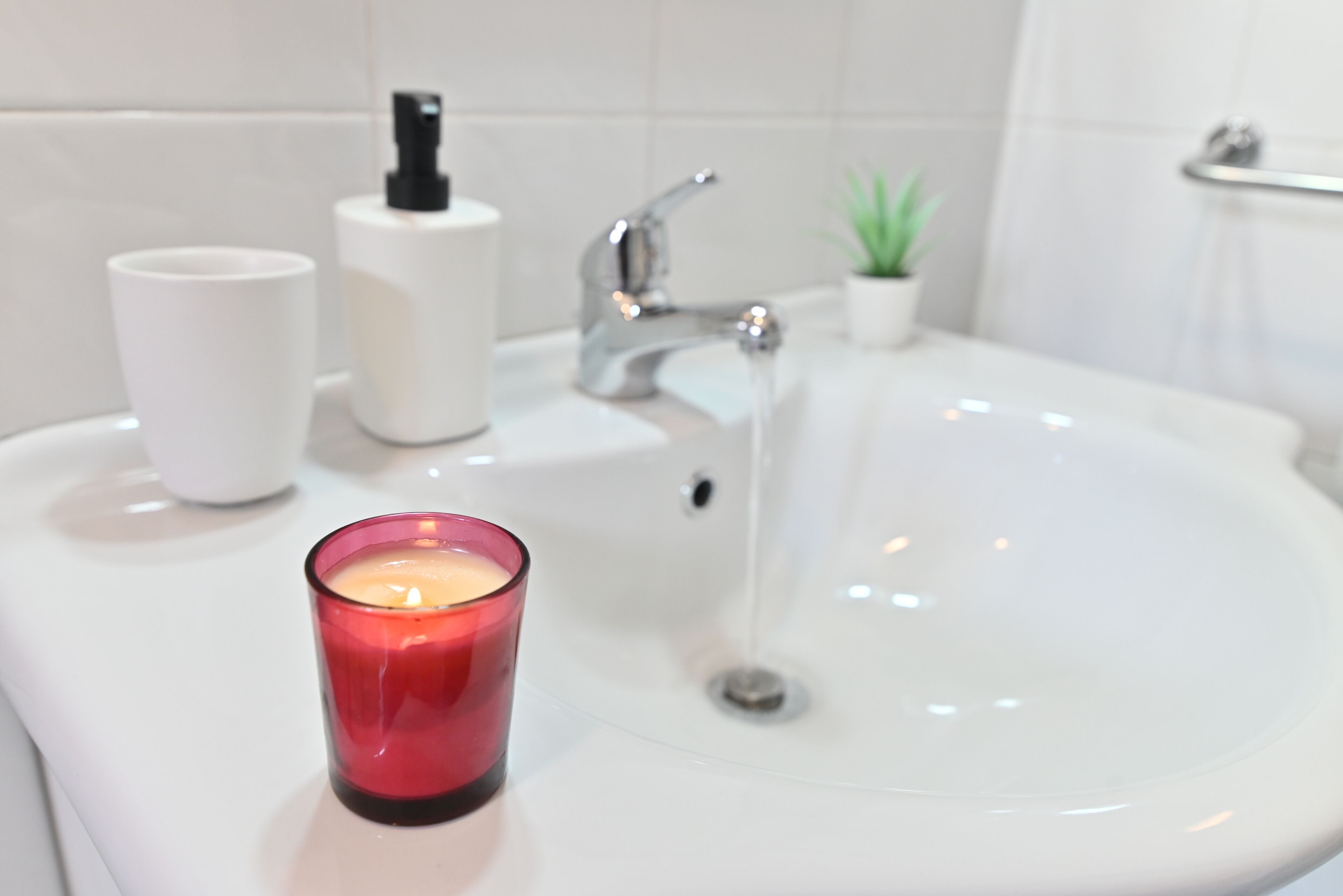 Un lavabo de salle de bain avec une tasse blanche, une bougie rouge et une petite plante en pot.