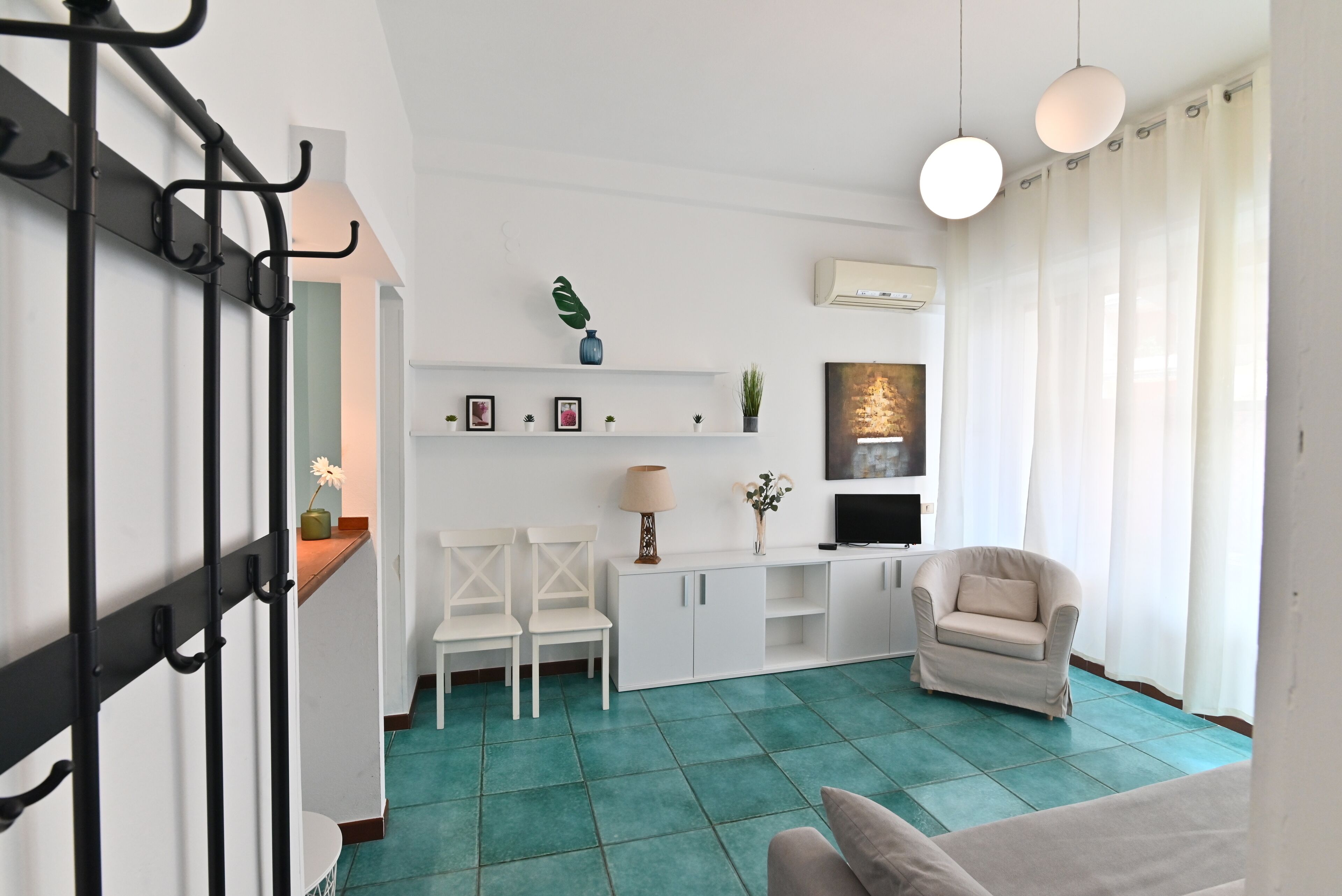 Una sala de estar con piso color turquesa, muebles blancos, un televisor y una planta en la pared.