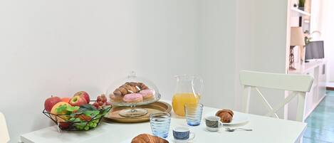 Una mesa de desayuno con croissants, una cesta de fruta, un jarro de zumo de naranja y una taza de café.
