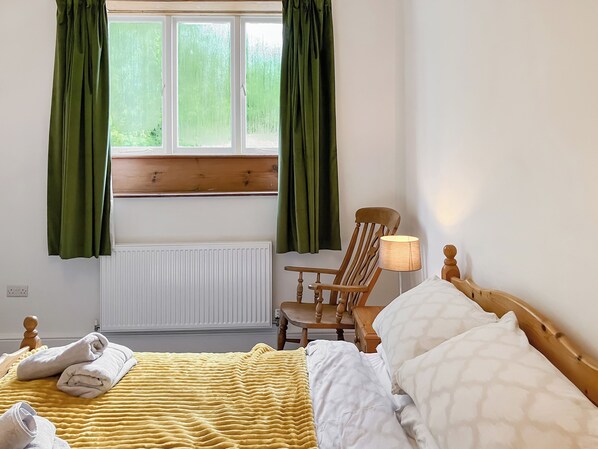 A hotel room with a bed, a chair, a lamp, and a window with curtains.