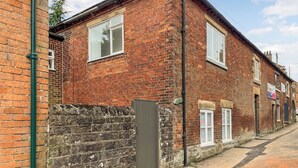 A two-story brick building with a white window, a door, and a small garden area. - Coldwell Street Cottage (Wirksworth)