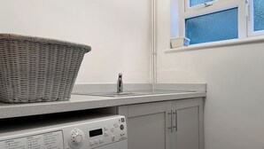 A compact laundry area with a washing machine, a drying rack, and a window with a view. - Coldwell Street Cottage (Wirksworth)