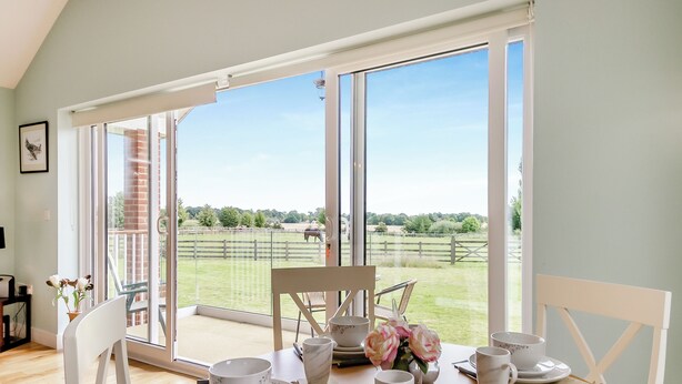 A dining area with a table set for four, large windows, and a view of a fenced outdoor area with a horse. - An ideal destination for relaxation, comfort and immersion in nature’s beauty. (Old Buckenham)