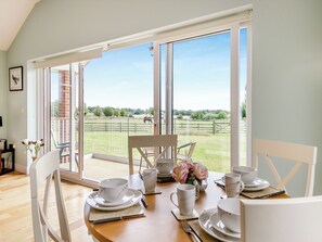 Un coin repas avec une table dressée pour quatre personnes, de grandes fenêtres et une vue sur un espace extérieur clos où se trouve un cheval.