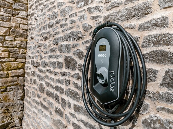 An electric vehicle charging station with a cable coiled around it, mounted on a stone wall.