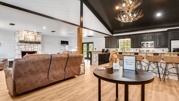 A spacious living area with a fireplace, a sofa, a dining table, and a kitchen with dark cabinets and a stone accent wall.