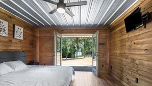 A modern bedroom with a large bed, a ceiling fan, and a TV mounted on the wall.