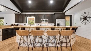 A modern kitchen with dark cabinets, a large island with bar stools, and a compass wall decoration.