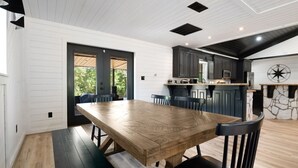 A modern kitchen with dark cabinets, a large wooden table, and a stone accent wall.