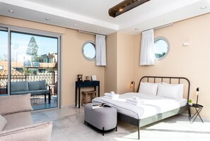 A modern bedroom with a bed, a desk, a chair, and a balcony with a view of buildings and a tree. - KEDEM - By Beach Apartments TLV (Tel Aviv)