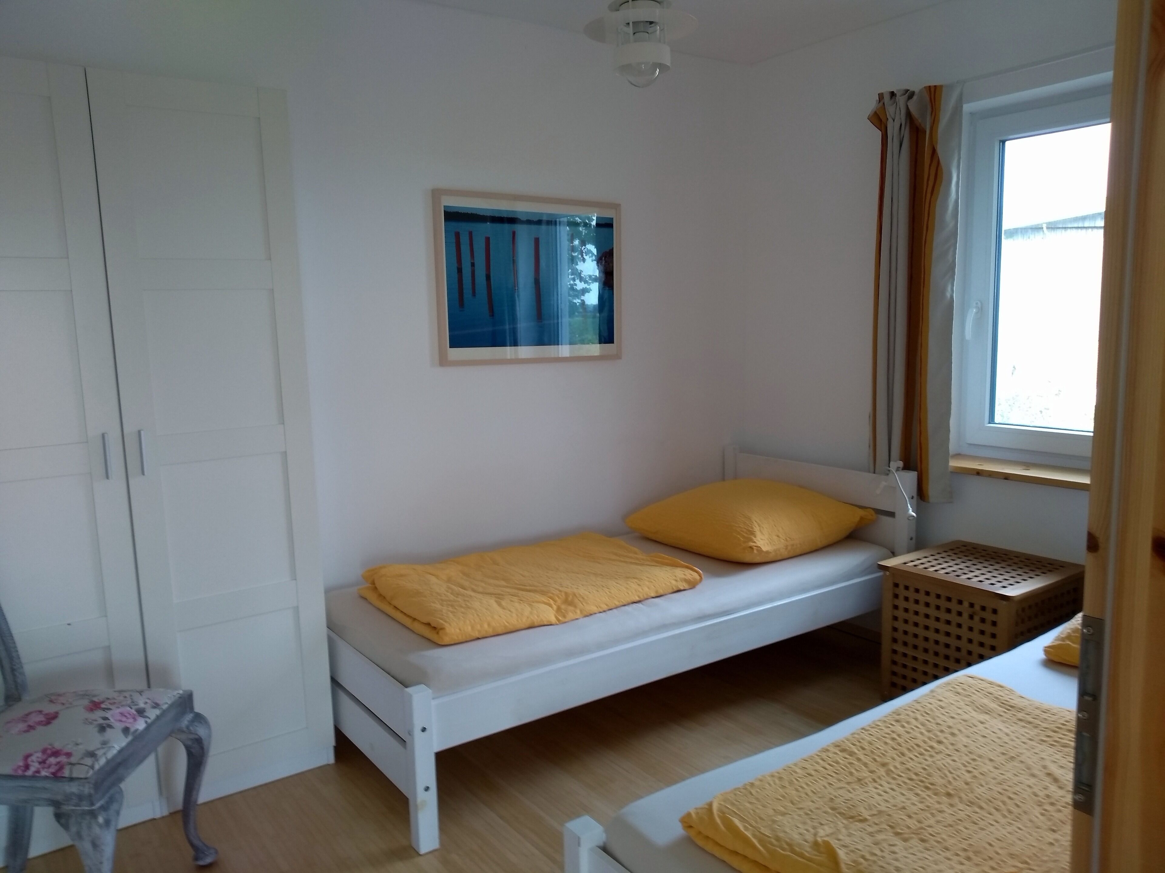 Een slaapkamer met een enkel bed, een stoel, een klein tafeltje en een raam met gordijnen.