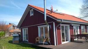 A red house with a sloped roof, a chimney, and a wooden deck.