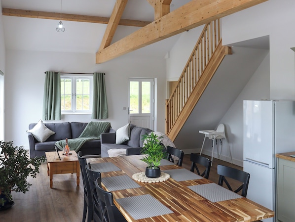 A modern interior with a dining table, chairs, a sofa, a staircase, and a refrigerator.