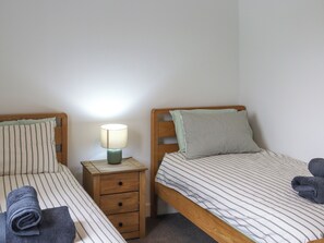 Deux lits simples avec une literie à rayures, une table de chevet avec une lampe et une tête de lit en bois.