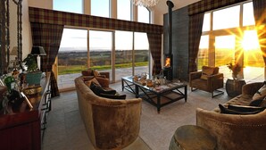 Un salon spacieux doté d’une cheminée, de grandes fenêtres et offrant une vue sur la campagne.