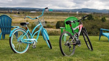 Two bicycles, a blue one and a red one, parked on a grassy field with chairs and a green structure in the background.