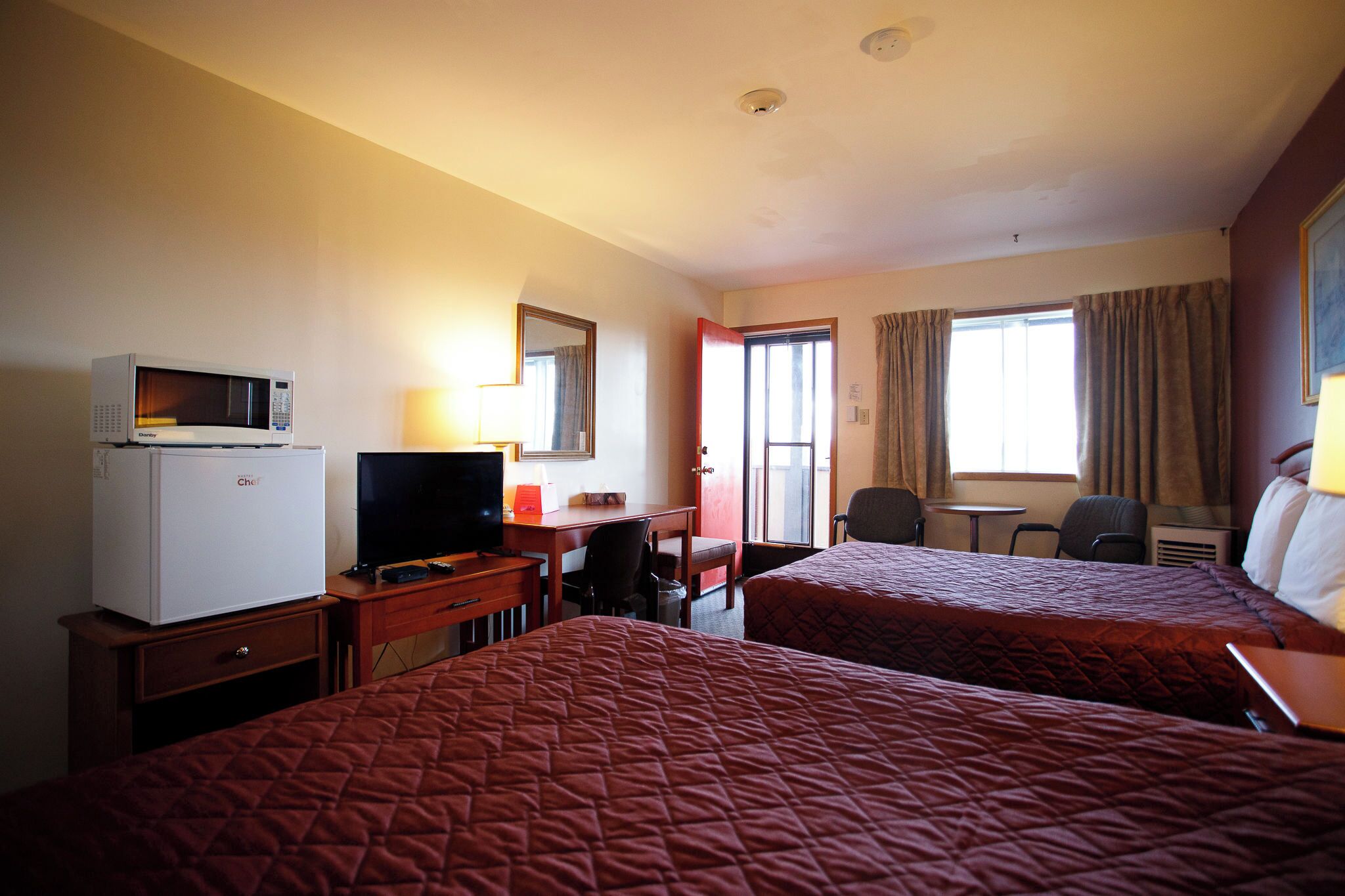 Habitació d'hotel amb dos llits, una taula de treball amb un ordinador, un televisor, microones i una finestra amb cortines.